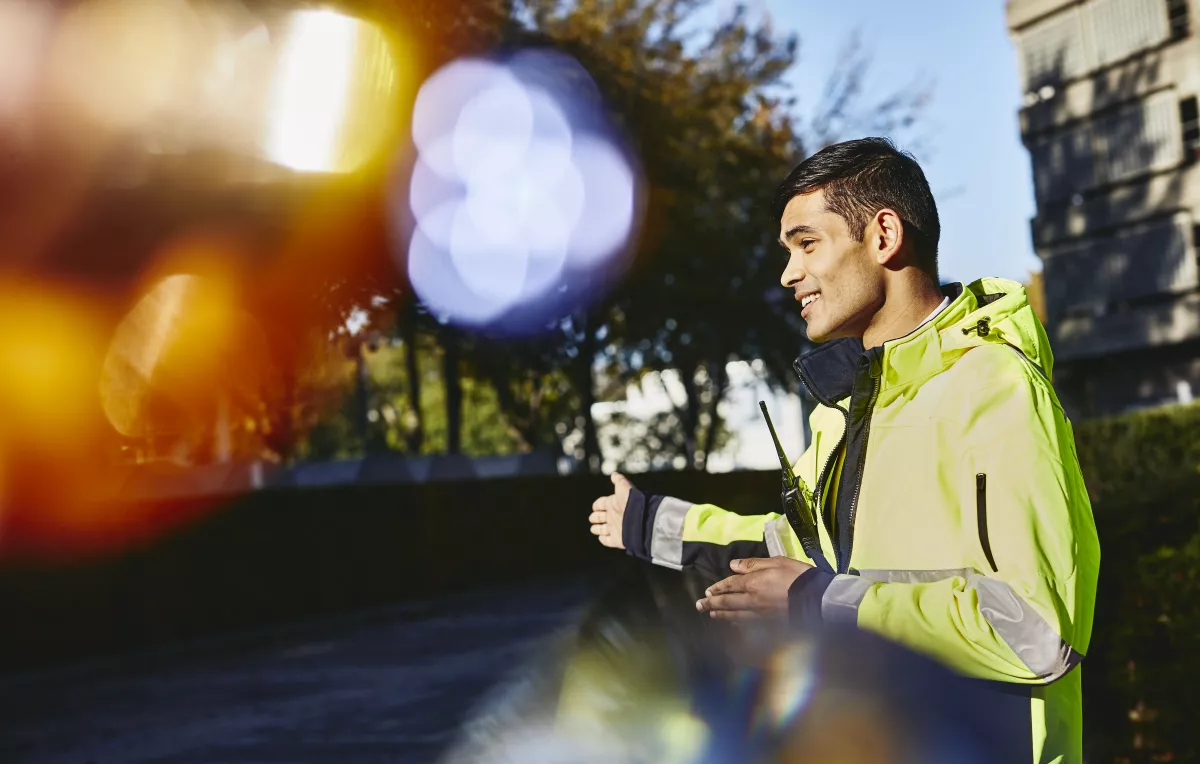 in de foto is er een man in een fluojas die richting aangeeft aan iemand anders op straat. De foto is een inleidende foto rond het deel Werkplekleren