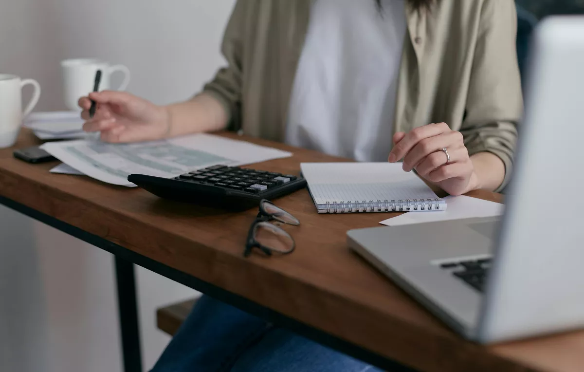 Een vrouw zit aan het tafel en ze is bezig met een paar documenten, laptop en een rekeningmachine